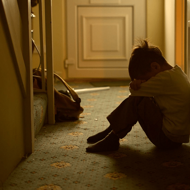 sad child with his head between his legs left alone at home