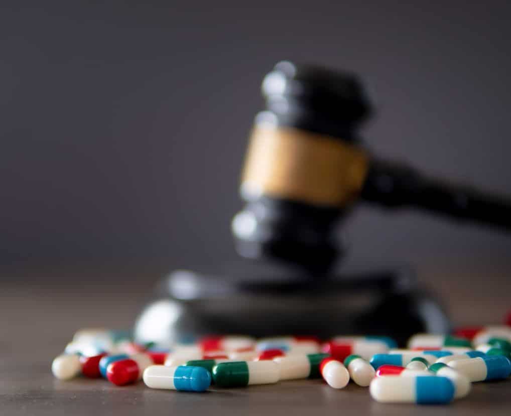 Closeup image of colorful medicine pills and judge gavel on table.